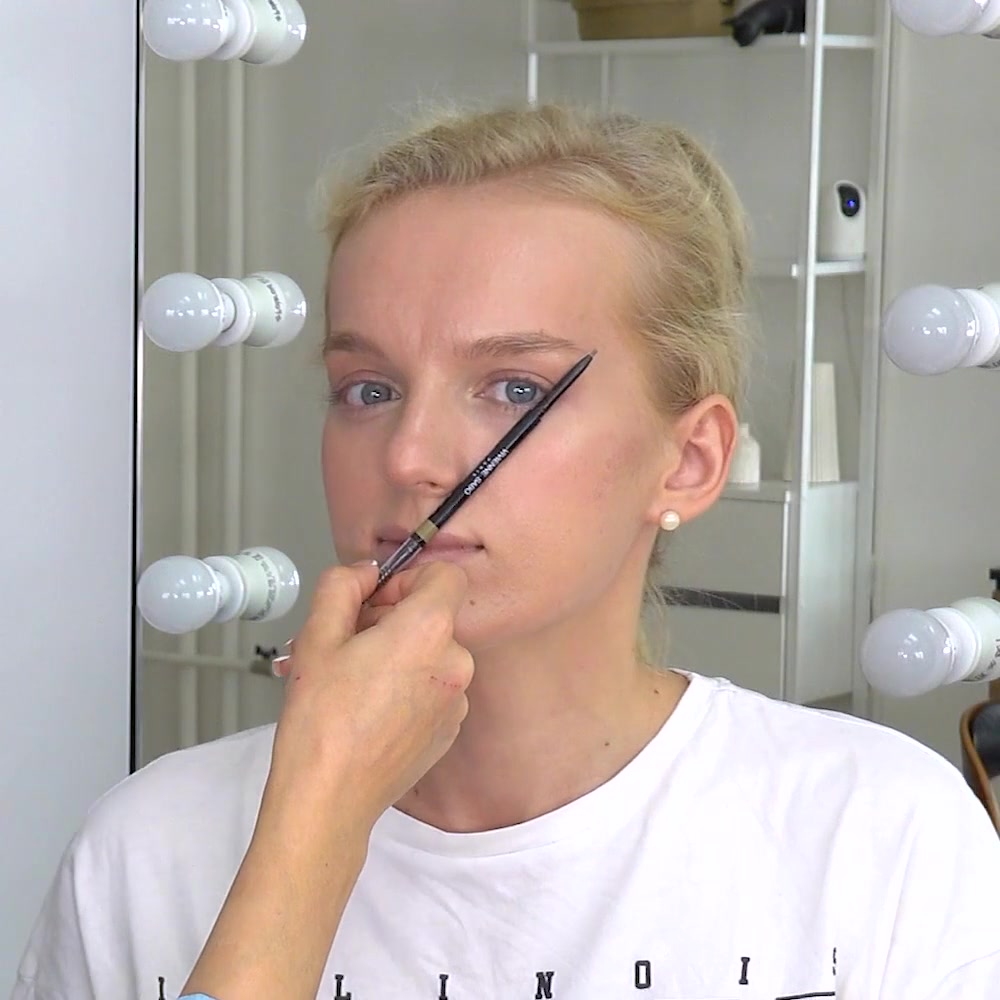 An instructor holds a brow pencil at the model's brow to check shape