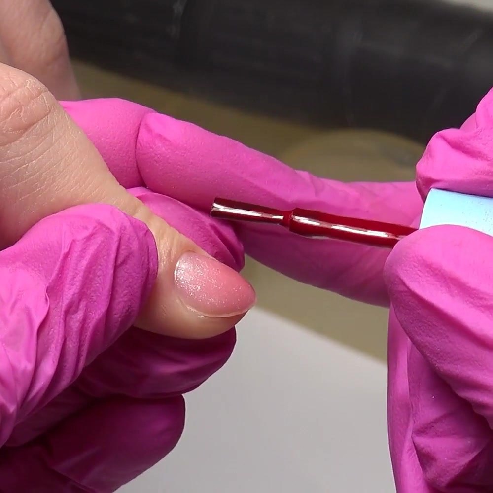 La primera capa fina de gel polish rojo se tira suavemente hacia el borde libre