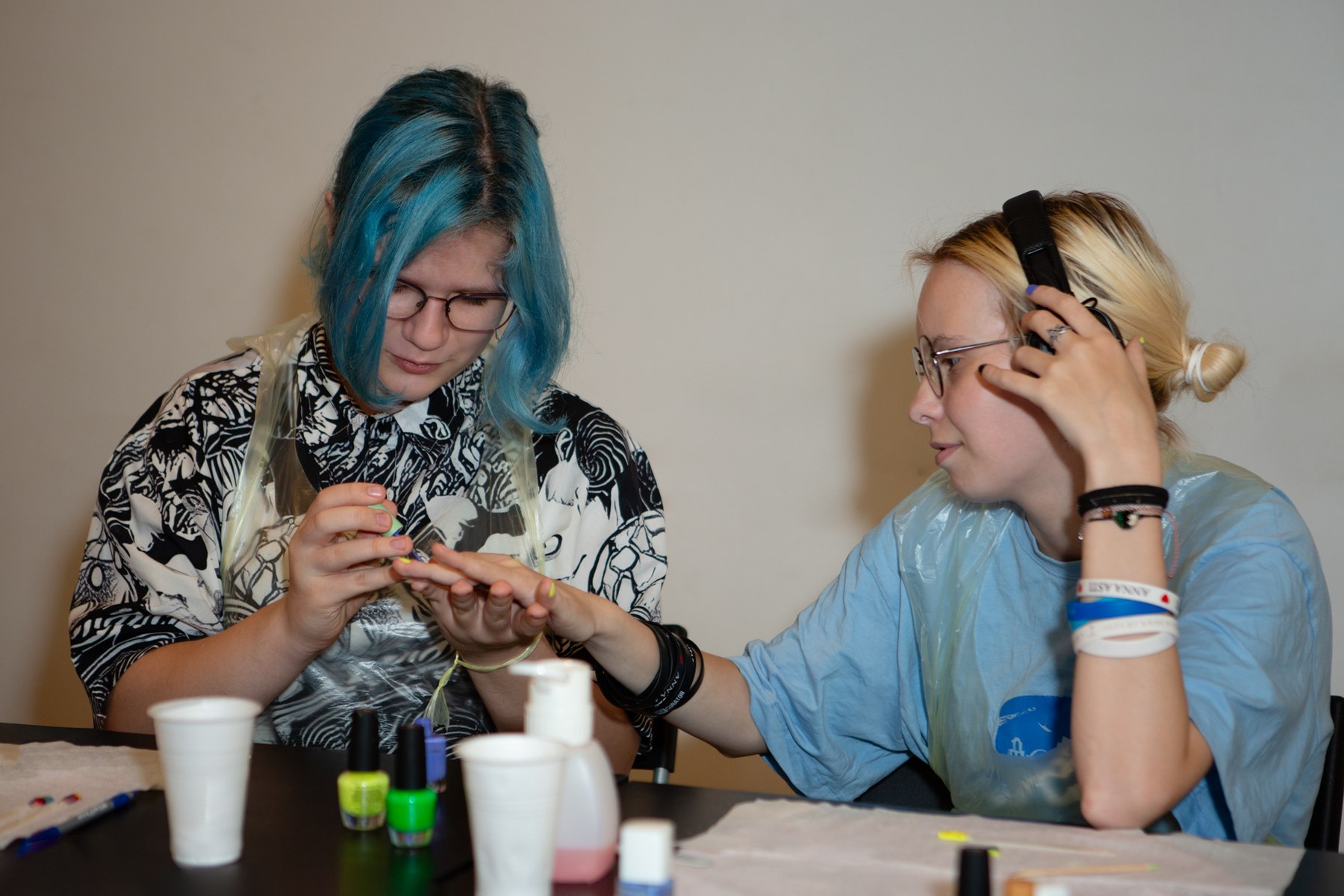 Teen applying a thin coat of color to another student’s natural nail