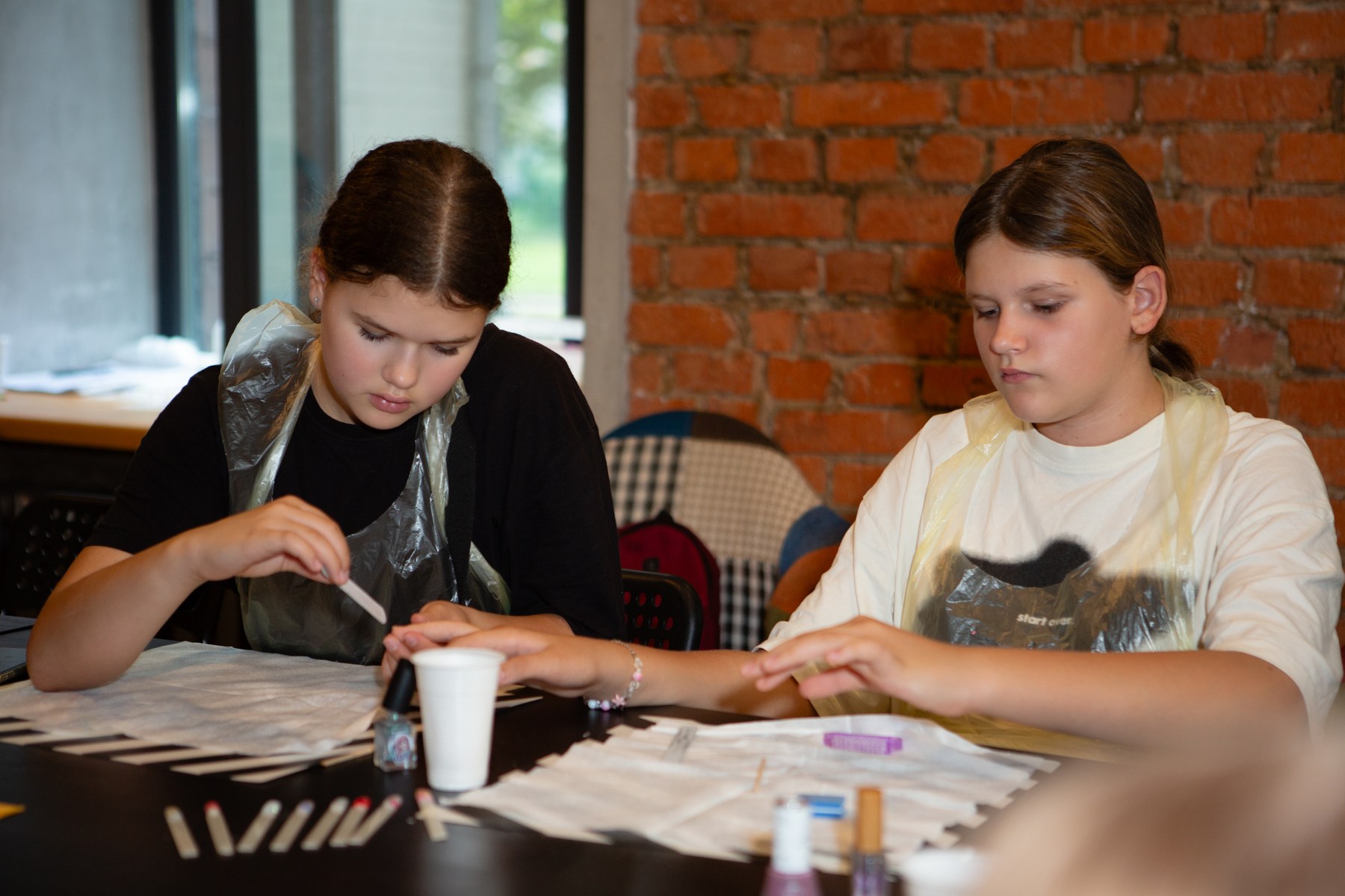 Teen filing another student’s natural nail before applying polish