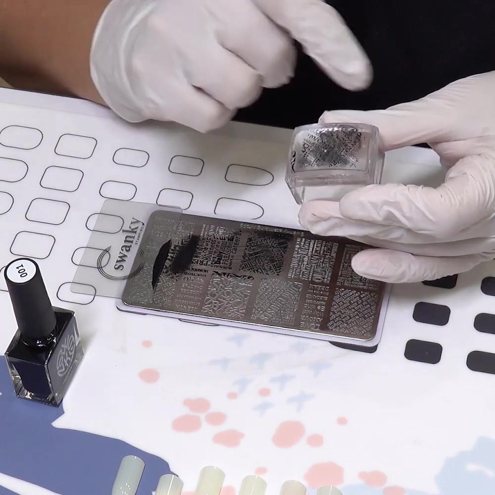 Un estampador transparente sostiene un patrón negro nítido recogido de una placa de estampado de uñas grabada