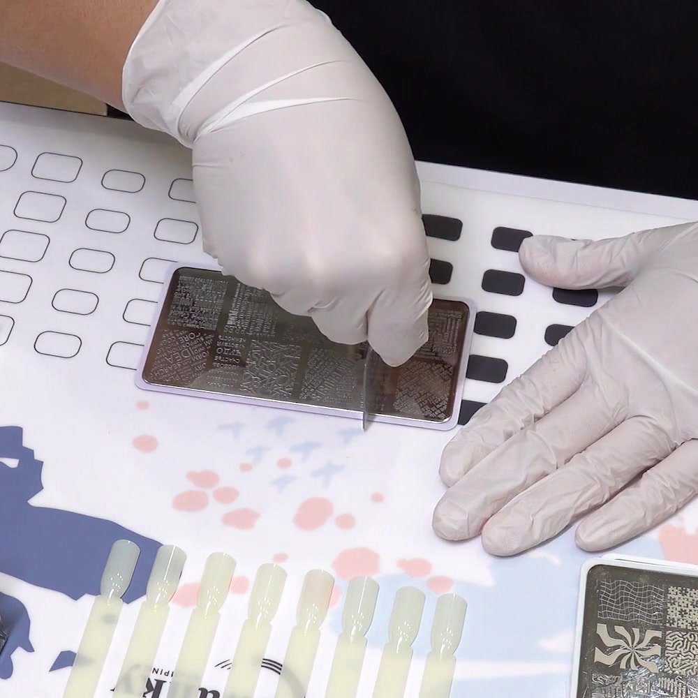 The scraper is held at an angle over the nail stamping plate