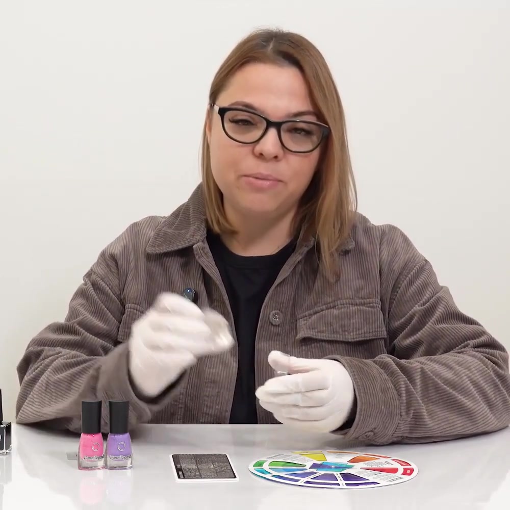 The instructor shows a clear silicone nail stamper used to pick up engraved designs
