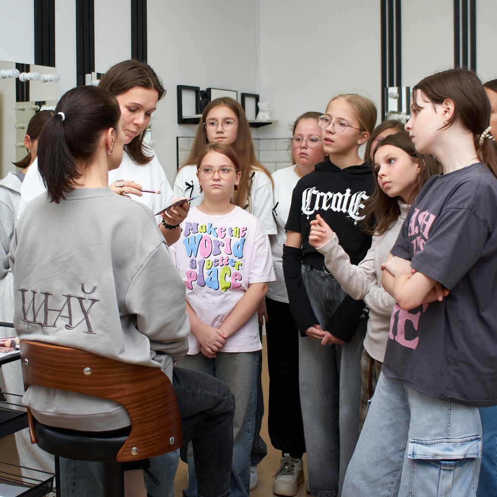 A makeup instructor explains a demonstration to a group of teen students