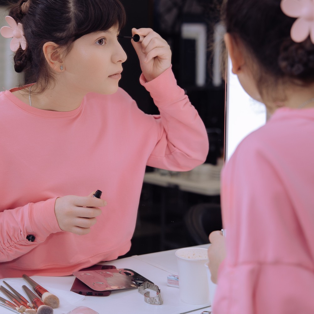 A student practices applying mascara while looking into a mirror