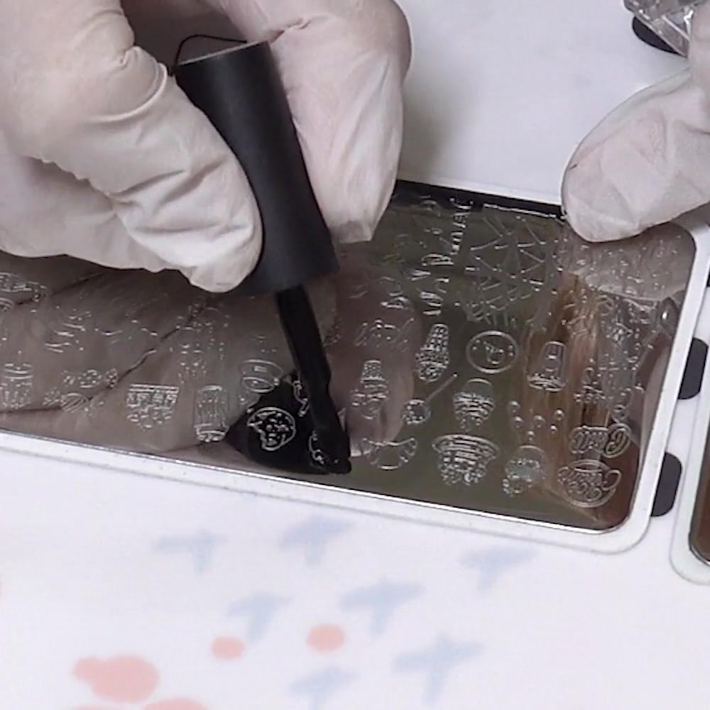 Black stamping polish is brushed over an ice cream outline on a metal plate