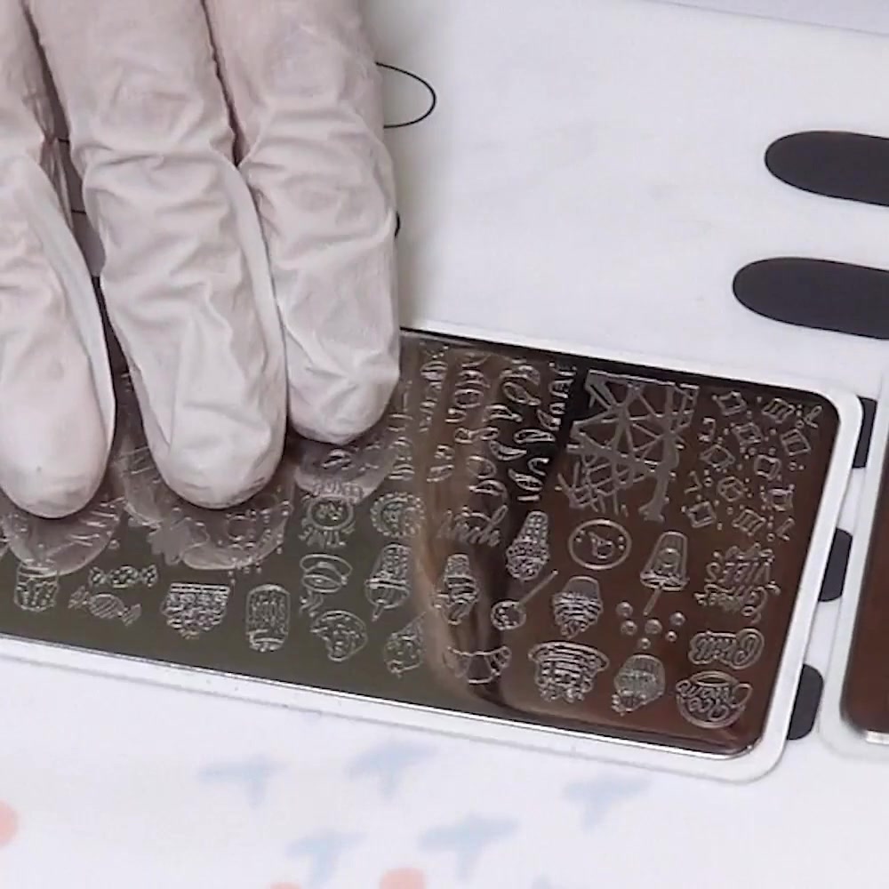 A gloved hand points to small dessert outlines on an engraved nail stamping plate